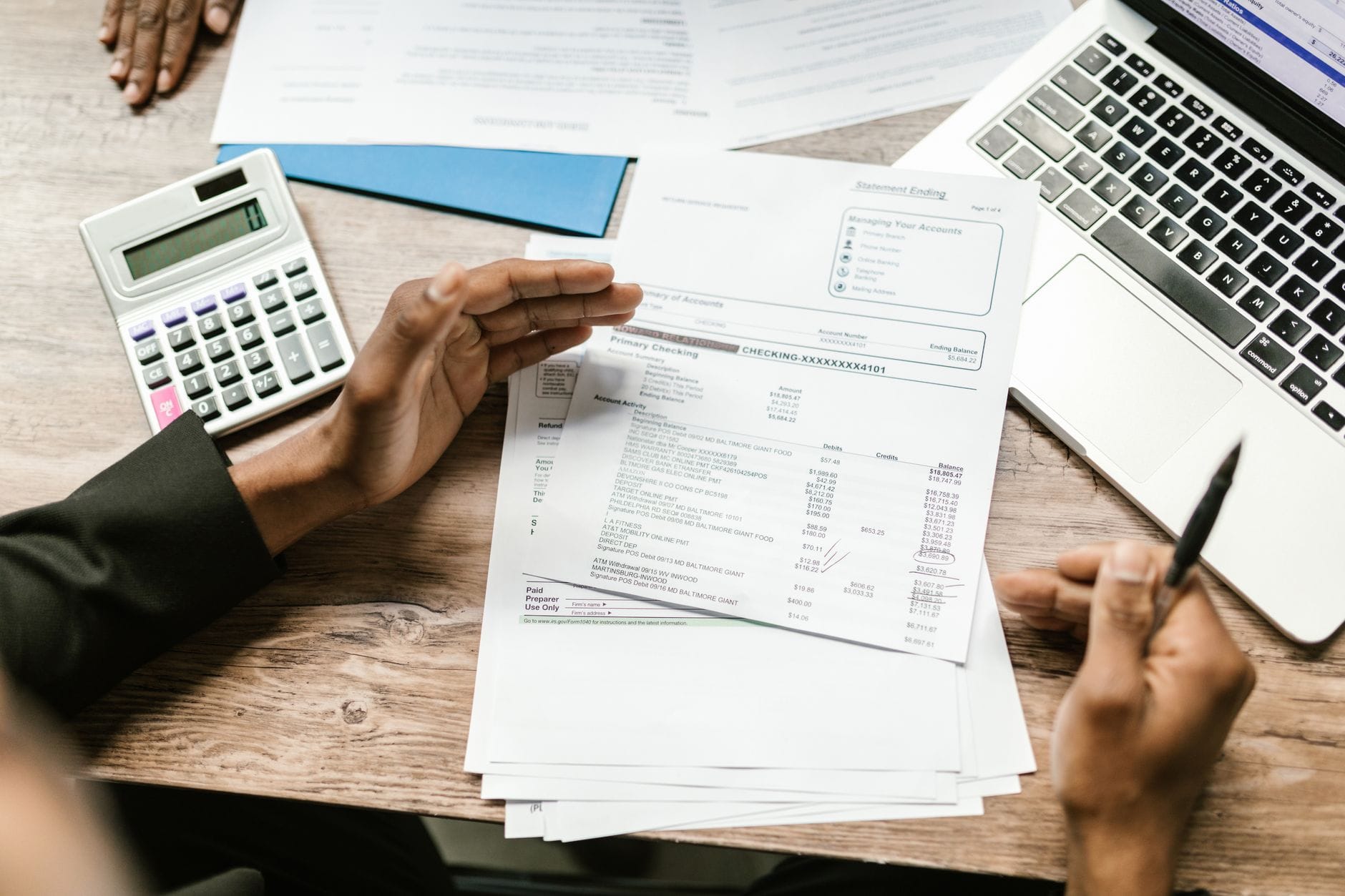 Des mains posées sur des relevés bancaires étalés sur une table de cuisine