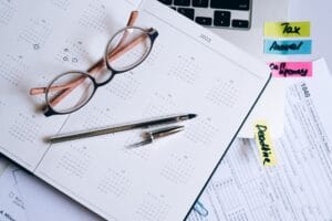 Un bureau clair avec un agenda ouvert, une calculatrice et quelques factures posées à côté