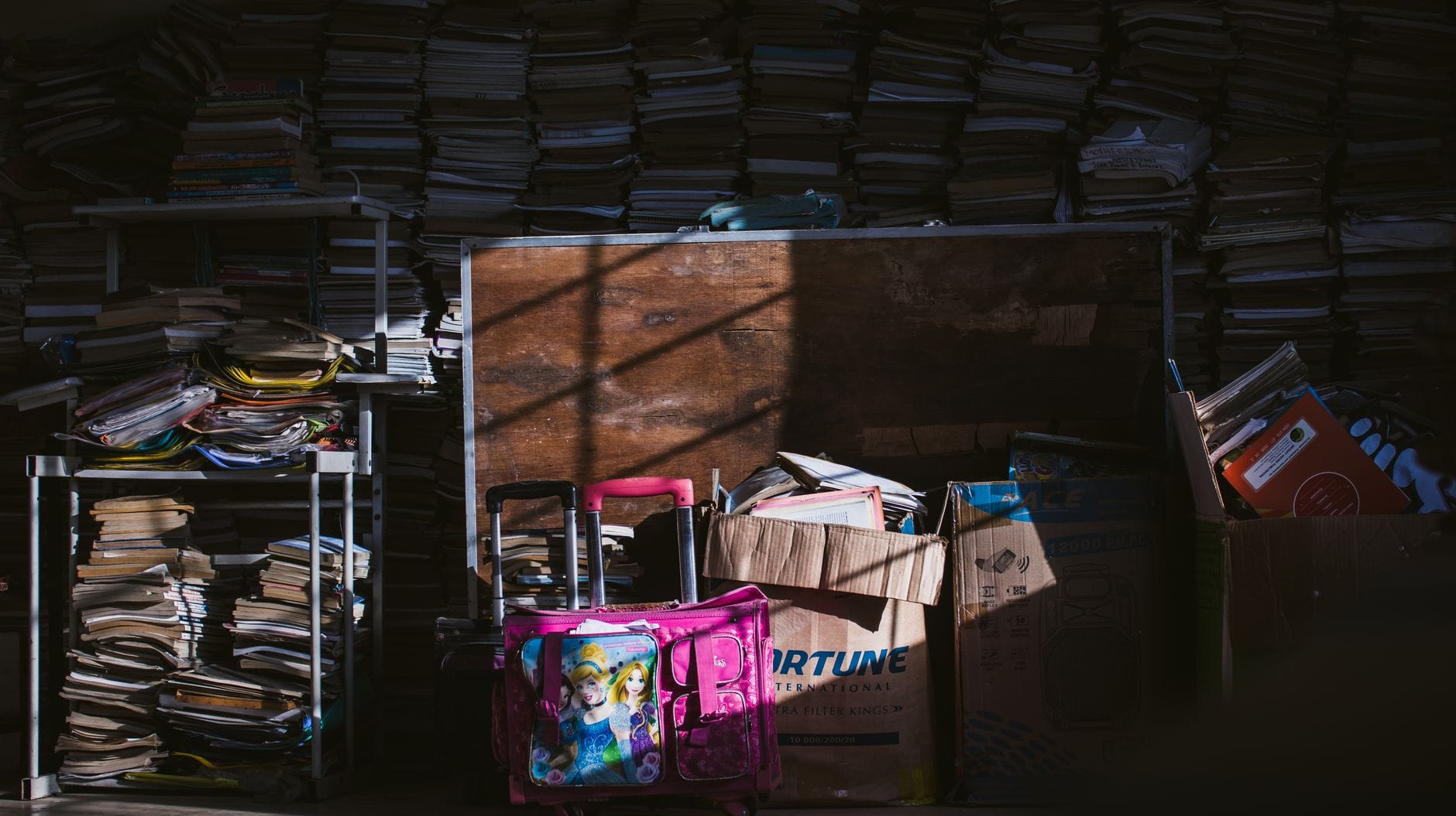 Un carton de papiers ouvert posé au sol à côté d'un bureau, avec des classeurs à côté.