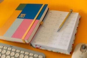 Agenda de cabinet libéral ouvert sur un bureau ensoleillé, à côté d'un carnet de comptes, avant les vacances d'été