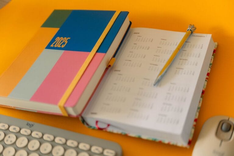 Agenda de cabinet libéral ouvert sur un bureau ensoleillé, à côté d'un carnet de comptes, avant les vacances d'été