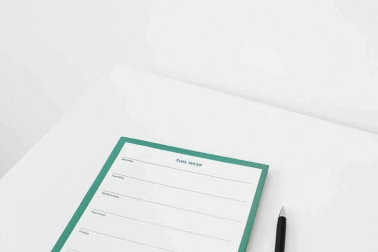 Un agenda papier ouvert sur un bureau clair, avec un téléphone et un stylo posés à côté.