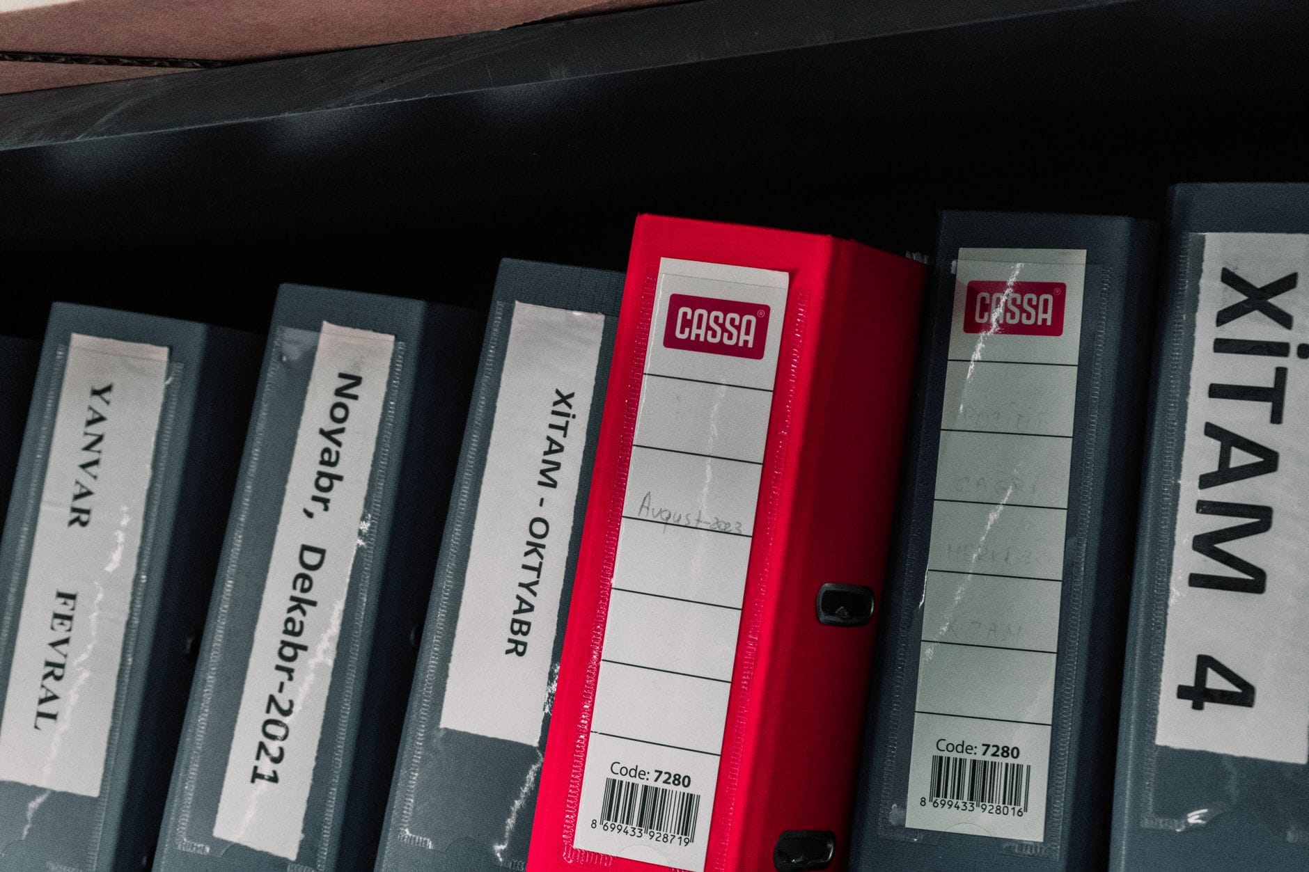 Une pile de factures et de relevés bancaires posée à côté d'un classeur ouvert sur un bureau.